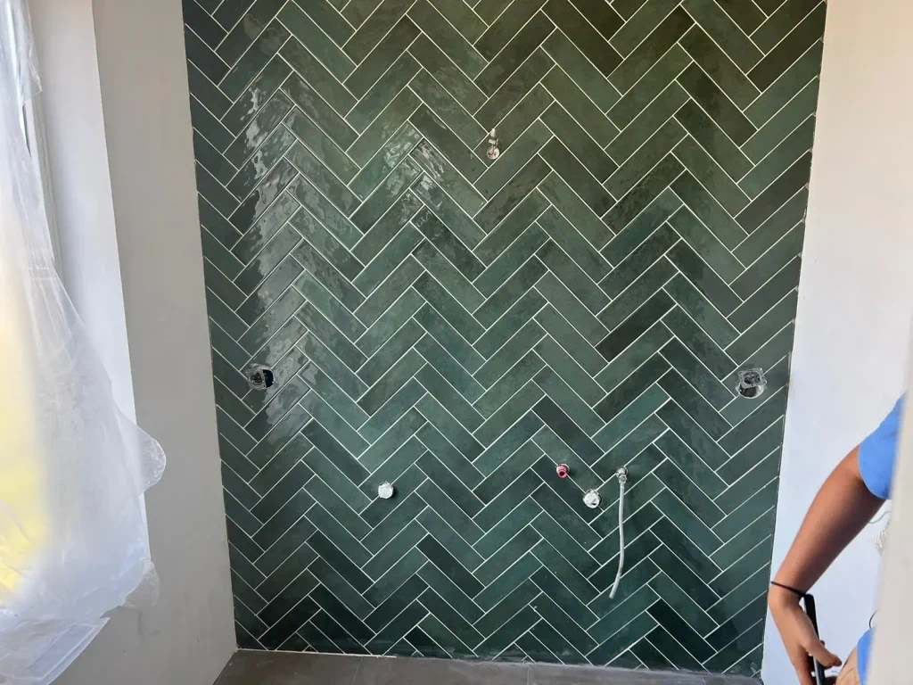 Groen tegelwerk in visgraatpatroon op een wand met aansluitingen voor sanitair.