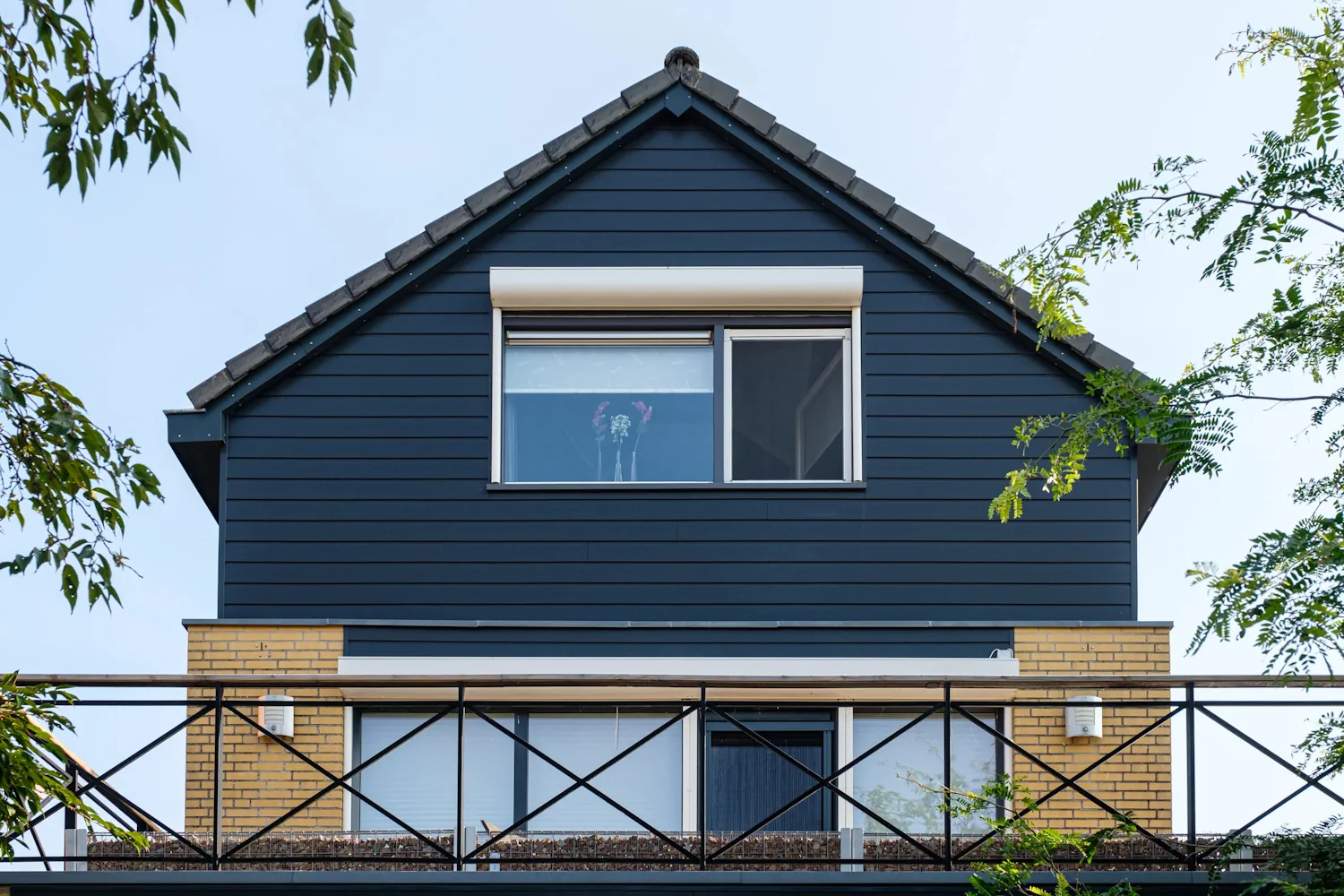 Woning met donkere Keralit gevelbekleding, een raam op de verdieping en een balkon aan de voorzijde.