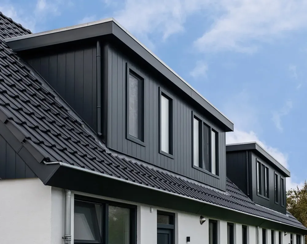 Woning met donkere Keralit gevelbekleding en meerdere dakopbouwen onder een blauwe lucht.