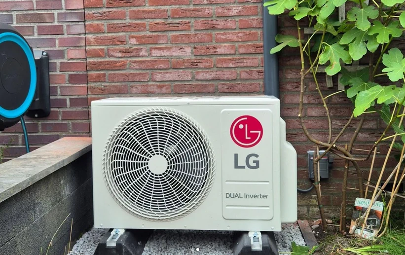 LG-airco-buitenunit tegen een bakstenen muur naast beplanting.