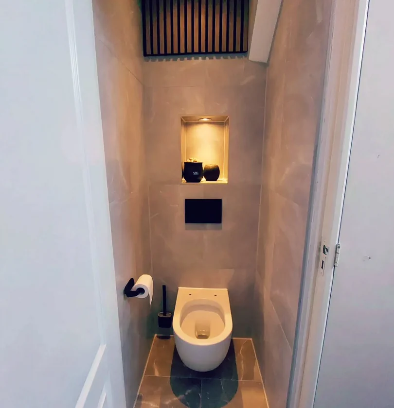 Sanitair met een hangend toilet, bedieningsplaat en nis in een betegelde toiletruimte.