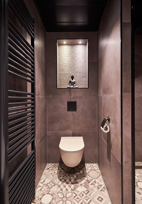 Toilet met donker tegelwerk, wandradiator en nis met mozaïekachterwand.
