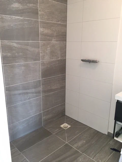 Tegelwerk in een badkamer met grijze wand- en vloertegels en een afvoerputje